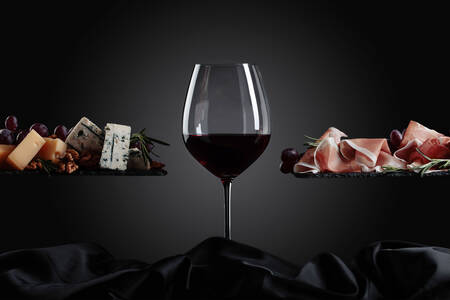 Bicchiere di vino, formaggio e prosciutto su sfondo nero